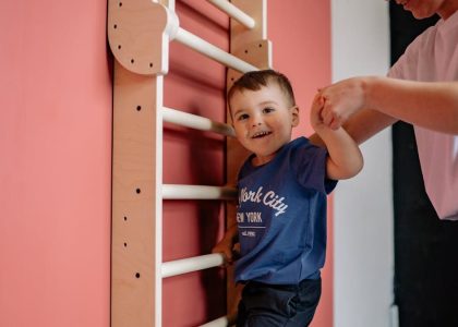 A smiling boy climbs a wooden ladder with a woman's assistance, embodying teamwork and joy indoors.