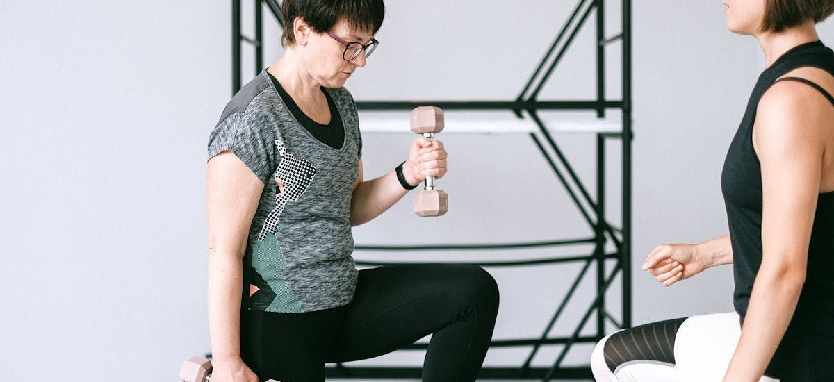 Elderly woman lifting dumbbells with guidance from a trainer indoors.